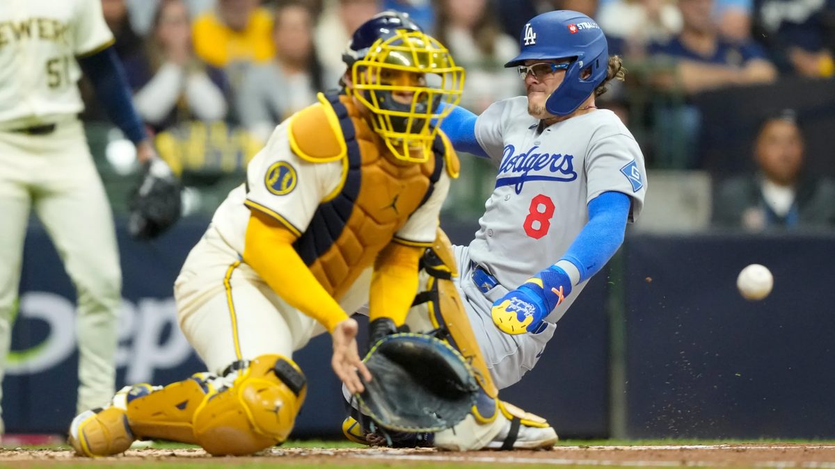 A Dodgers baserunner slides into home plate as the Brewers catcher reaches for the throw at American Family Field