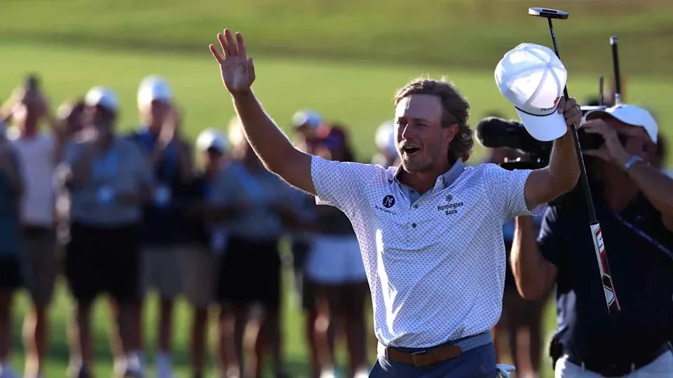 Austin Smotherman raises his arms and his cap in celebration on the 18th green as fans cheer behind him